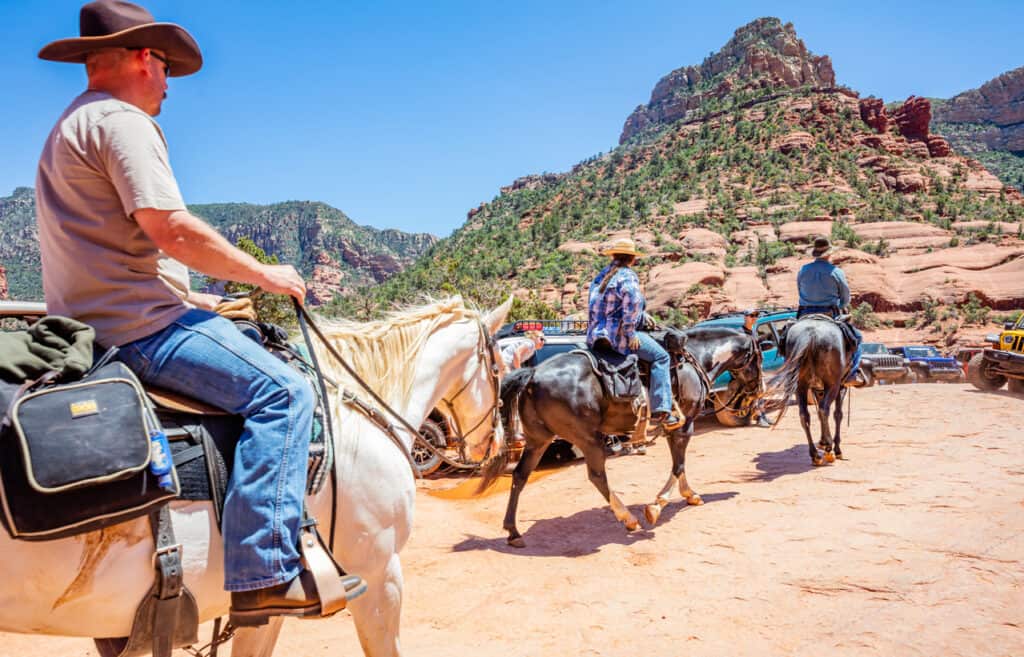 Sedona Arizona USA. May 25, 2019. People riding horses and 4X4 parked on terrain. Red orange desert landscape, clear blue sky, sunny spring day