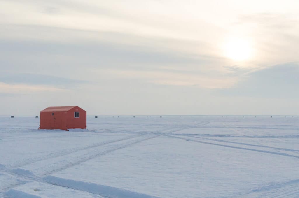 Orange Ice fishing huts on a frozen lake in Ontario at sunset showing tracks. Ice fishing in Ontario