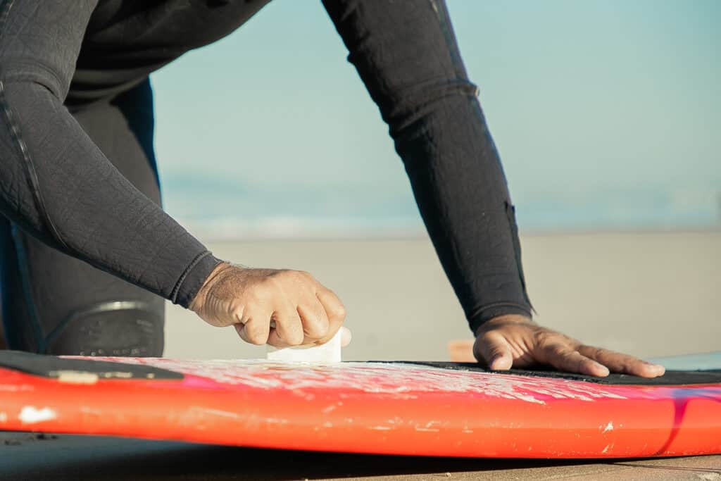 Male surfer in wetsuit waxing surfboard on sand on ocean beach. Cropped shot. Surfing and active lifestyle concept for surfing Nosara