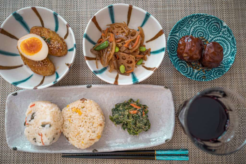 Best Food And Wine Tours For Foodies Over 55, this is in Japan. Presentation is integral to the dining experience. in this photo, four plates of uniquely Japanese delicacies are laid out along with dark Saki