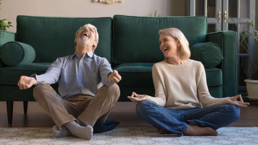 Laughing funny elderly spouses sitting in living room on floor in lotus position practice meditation distracted from yoga exercise joking feels overjoyed, healthy active lifestyle of retirees concept. one of my simple pleasures