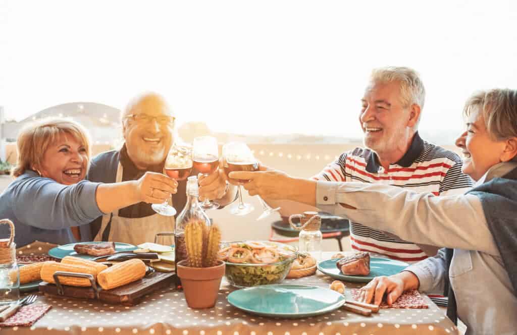 Happy senior dining and tasting red wine glasses in barbecue dinner party Lead picture for post Best Food and Wine Tours for Foodies Over 55
