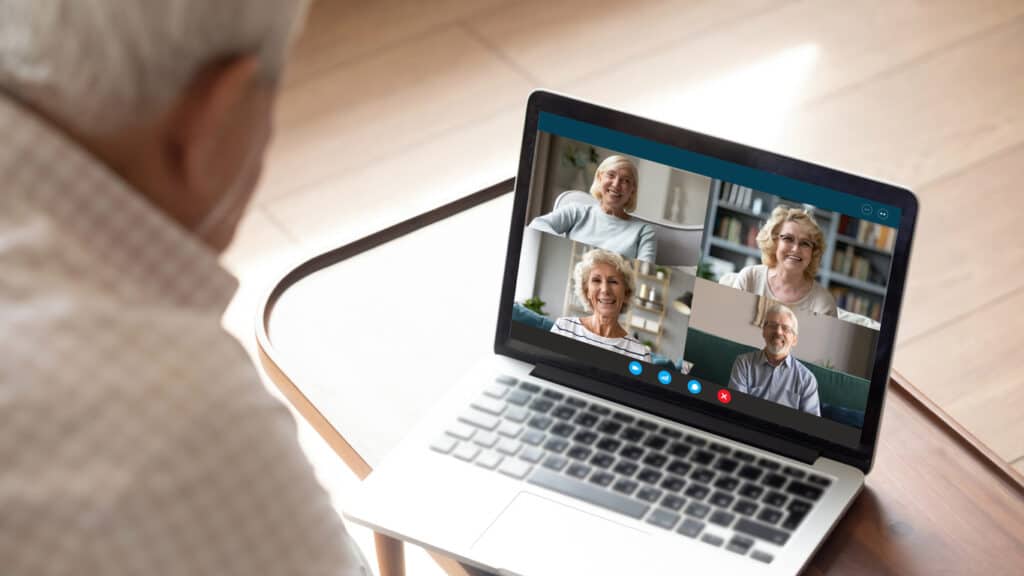 Older generation and modern technologies for virtual visual communication concept. Old man makes videocall talking with relatives or friends by video conference app, pc screen view over male shoulder. good for older solo travelers too