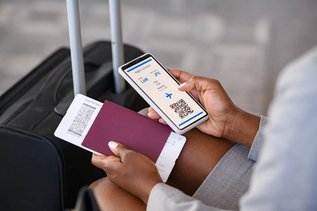 Person using helpful apps for older solo travelers for checking flight eticket on phone while holding passport and boarding pass.
