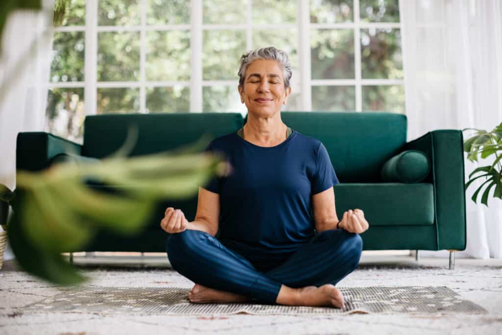 Senior woman meditating in lotus position at home, sitting on the floor in fitness clothing. Mature woman doing a breathing workout to achieve relaxation, peace and mindfulness. one of my favorite simple pleasures