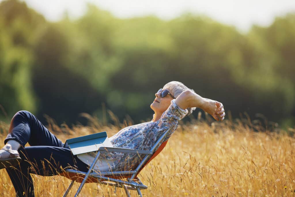 woman reading a book in a lawn chair in an open sunny field. Reading is my favorite simple pleasure.
