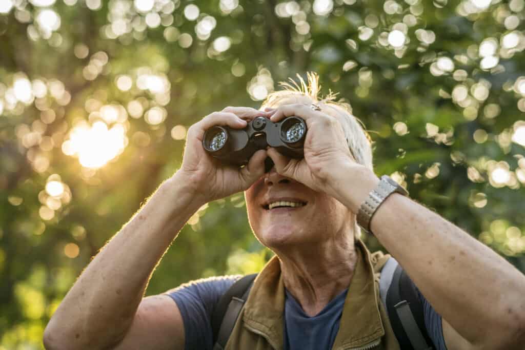 Elderly man watching birds with binoculars. Binoculars are essential for seeing the birds of Costa Rica. Photo iStock
