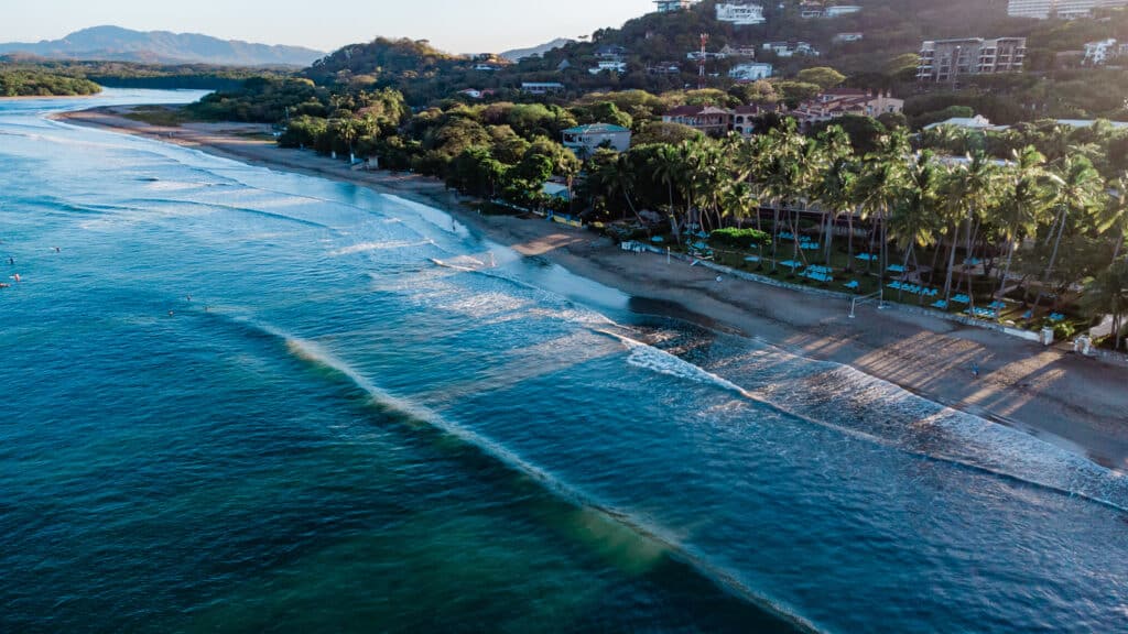 The sun rays break through the palm trees that line Tamarindo Beach, Costa Rica during a January sunrise. Tamarindo is a popular Costa Rican beach town known for its nightlife, beach vibes, and surfing. Photo, iStock