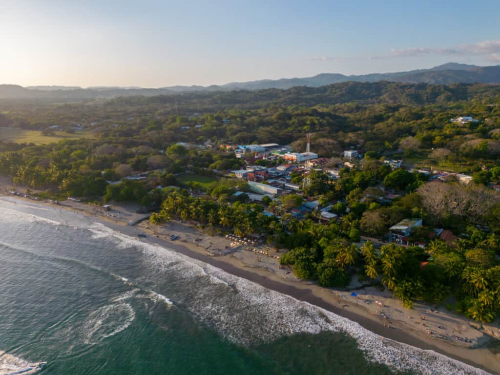 This picture was taken by a drone. It shows the small village of Samara at the pacific coast in the province of Guanacaste, Costa Rica. You can see the village in the back, the beach where tourists sunbathe and the green mountains. Rated as one of the best beach towns in Costa Rica Photo, iStock