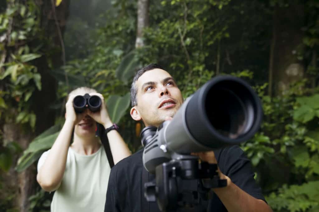 Woman with Binoculars and Man with Telescope in Rain Forest Jungle, looking at the birds of Costa Rica. Photo iStock.