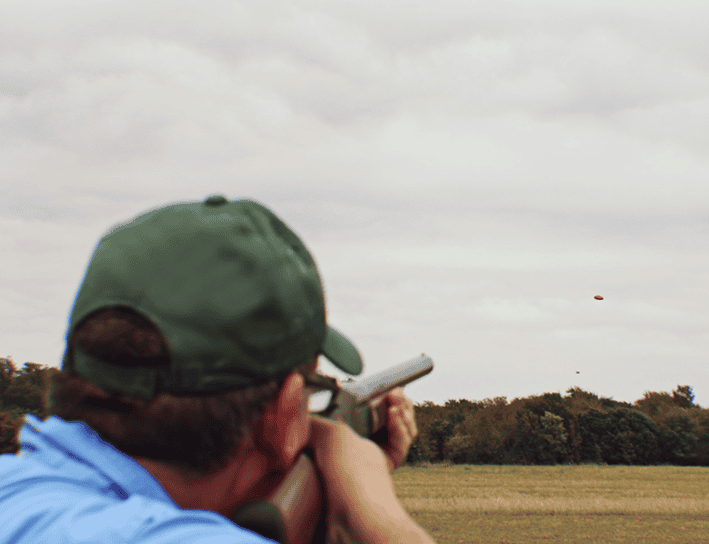 hobbies for retired men - shooting skeet. man in green hat shooting skket in an open field