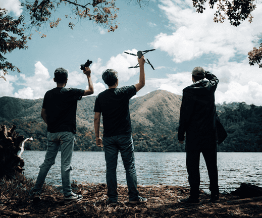 thre maale friends enjoying their drone flying hobby near a lake