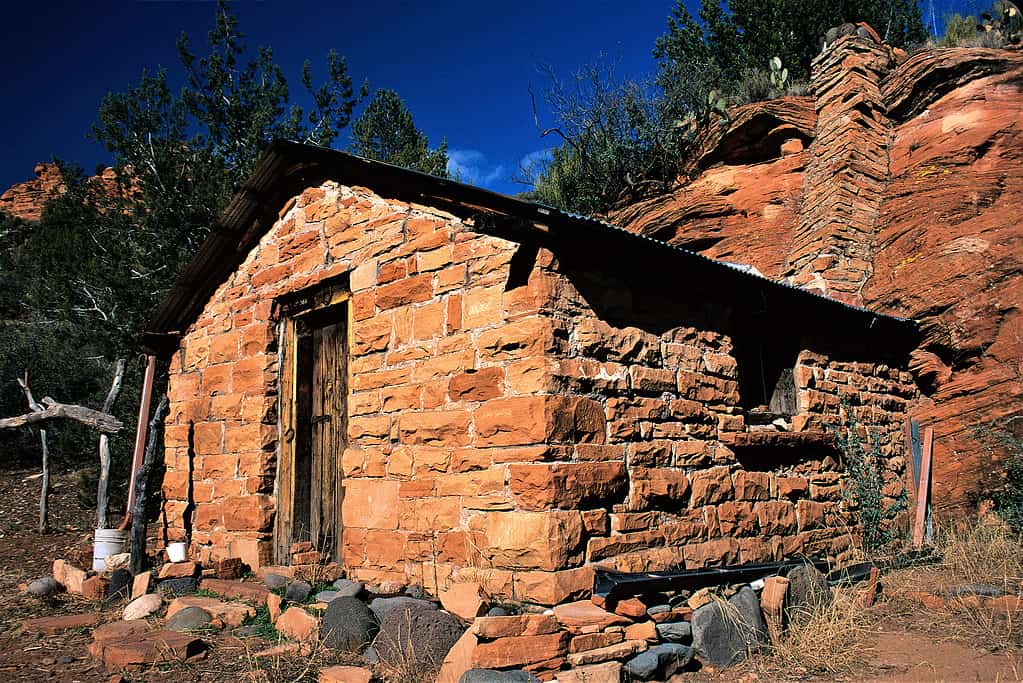 Historic Taylor Cabin in Sycamore Canyon Wilderness Sedona Arizona USA.  Probably the cabin is totally hand hewn.  Notice the chimney goes up the cliff face.  Clever.  Cabin next to Sycamore Creek.  Edge of Colorado Plateau. Unique things to do in Sedona Arizona - visit a ghost town